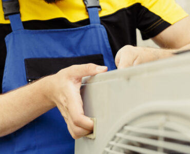 Close up of seasoned repairman installing condenser after replacing faulty unit. Adept worker commissioned to optimize air conditioner system performance, making sure it operates at maximum potential